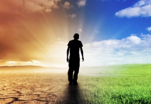 silhouette of man walking between barren soil and sunny sky