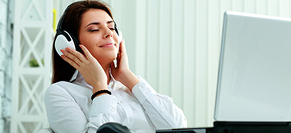 smiling woman executive happily listening to music on headphones while sitting at her desk