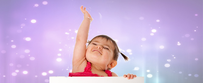 Happy little girl toddler with two pony tails with a big smile on her face and one hand up.