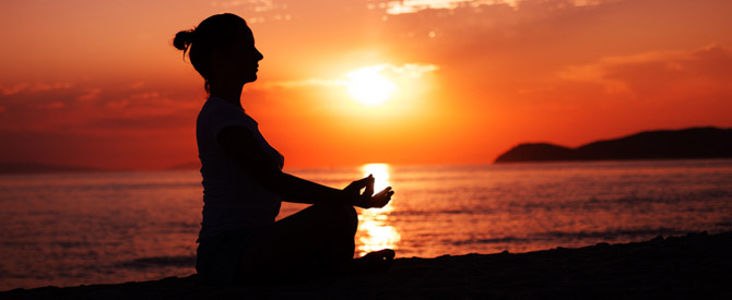 Silhouette of woman meditating on the beach at sunrise.