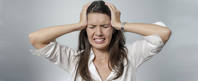 Stressed-out woman grimacing while placing her hands on the sides of her head.