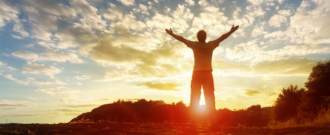 Silhouette of man reaching out to the sky at sunset.