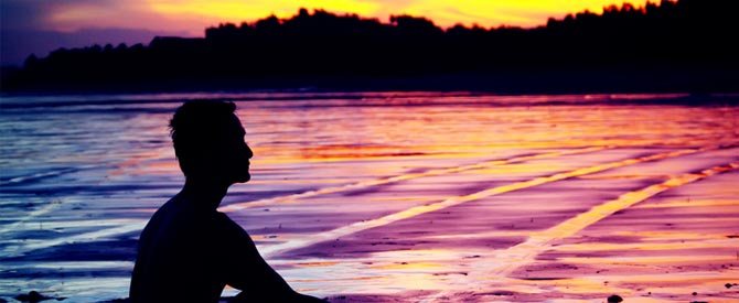 silhouette of man sitting by water