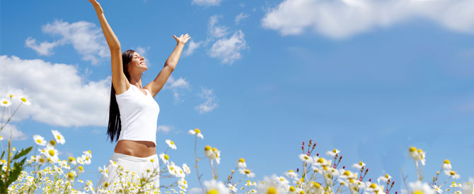 happy woman amidst flowers with arms raised and facing the sun