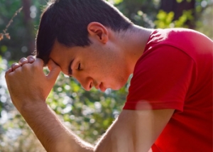 man with head on hands held in prayer