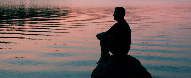 Silhouette of man sitting on a rock contemplating life.