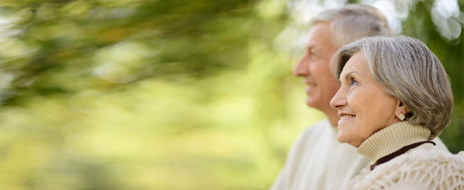 Smiling elderly couple sitting on bench in the park.