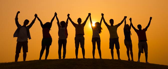 silhouettes of people holding hands above their heads at sunrise