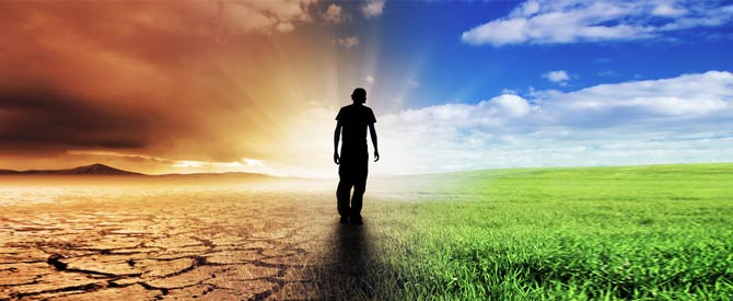 silhouette of a man walking down a path between dry parched land and lush green grass