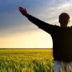 silhouette of a man in a grassy field at sunset with arms raised to surrender your worries and fears.