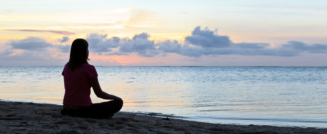 Silhouette of woman meditating on the beach at sunset.