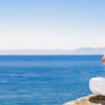 woman in white meditating near the blue ocean