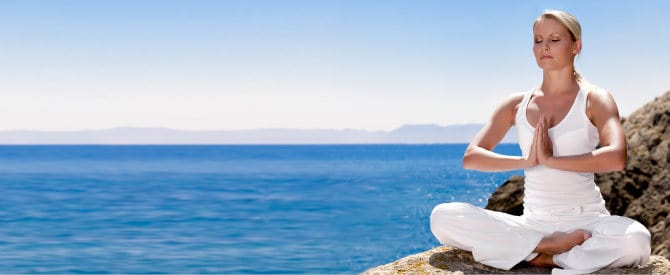 woman in white meditating near the blue ocean