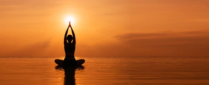 Silhouette young woman practicing yoga on the beach at sunset