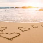 Hearts etched on a sandy beach at sunset representing the yoga fo devotion to the divine