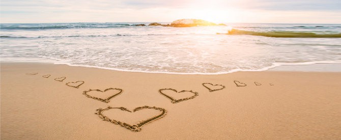 Hearts etched on a sandy beach at sunset representing things to give up to grow on the spiritual path.