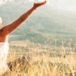 Woman with hands up facing the sky who has found the steps to a happier life.