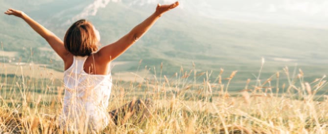 Woman with hands up facing the sky who has found the steps to a happier life.