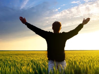 Man with inner wealth in fields with hands raised in wonderment of nature. 