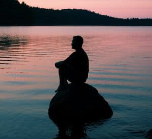 silhouette of man sitting on a rock at sunset reflecting on his inner growth.
