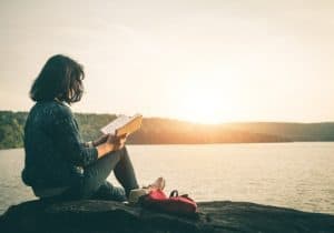 woman reading a book by a lake showing self study brings inner maturity