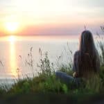 Woman sitting by a lake looking out at the sunset representing how to cultivate detachment