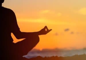 person meditating at sunset showing how to witness the thoughts and overcome anger