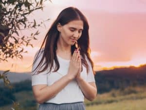 woman with hands in prayer outdoors